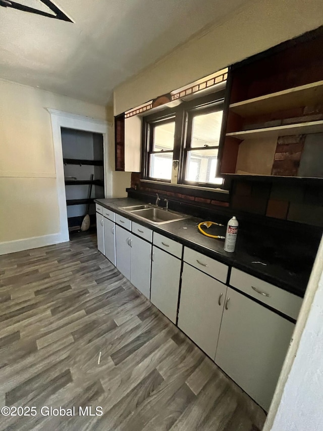 kitchen with baseboards, a sink, dark countertops, dark wood-style floors, and white cabinets
