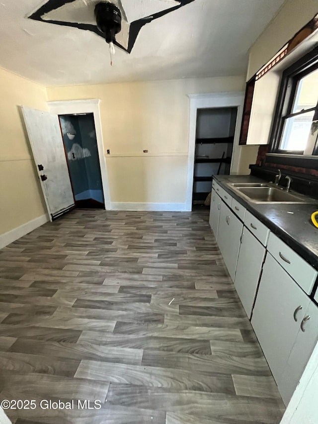 kitchen featuring white cabinets, baseboards, ceiling fan, dark countertops, and a sink