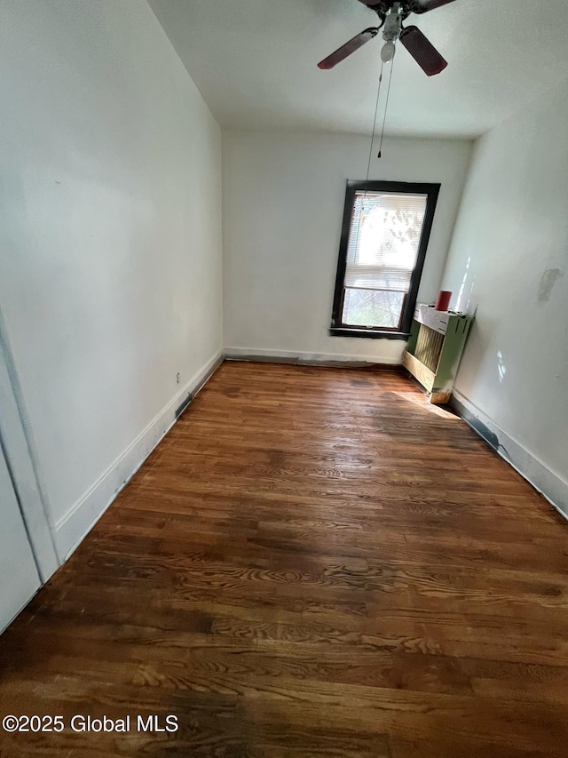 empty room featuring baseboards, wood finished floors, a ceiling fan, and radiator