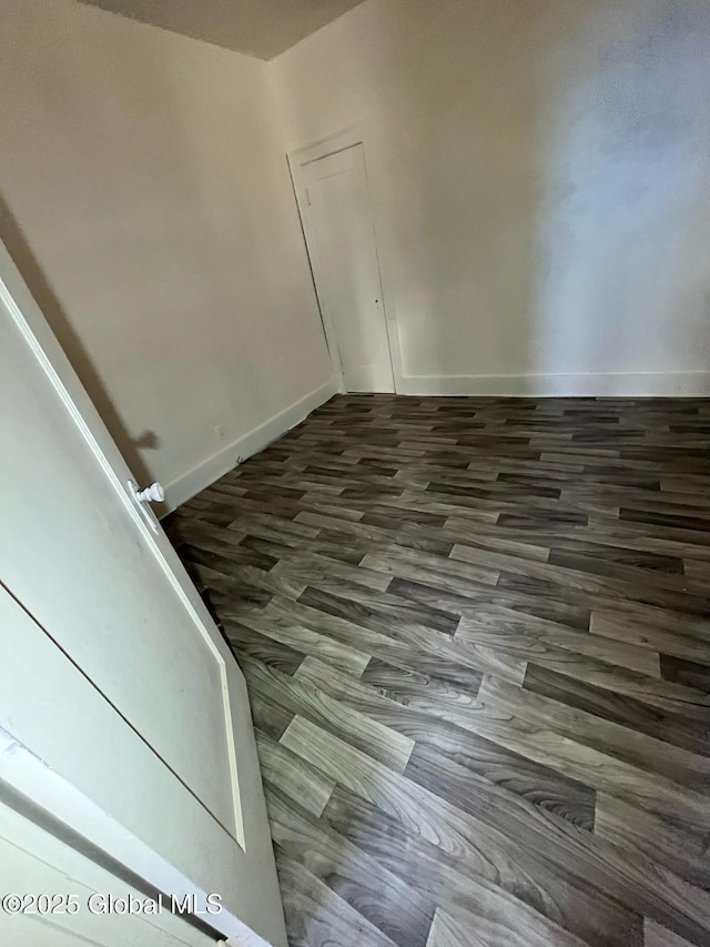 unfurnished room featuring baseboards and dark wood-type flooring