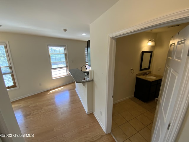 corridor featuring baseboards, recessed lighting, light wood-style floors, and a sink