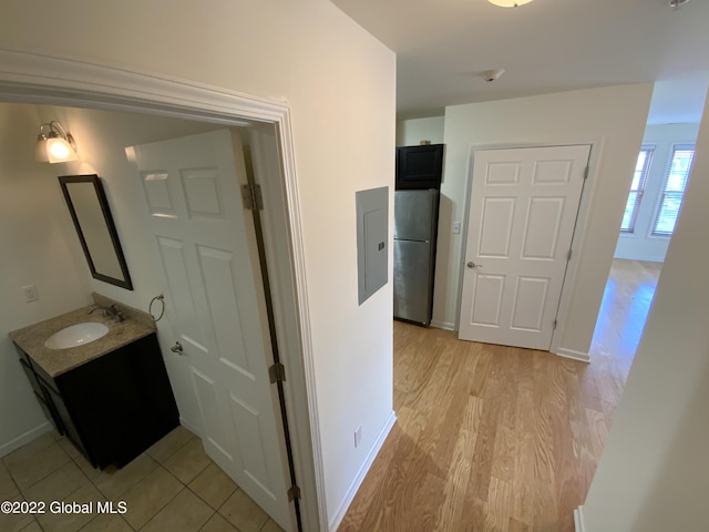 corridor with baseboards, light wood-style flooring, and a sink