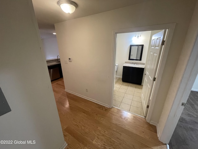 hallway featuring baseboards, a sink, and light wood-style floors