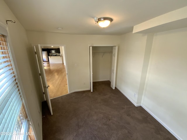 unfurnished bedroom featuring freestanding refrigerator, a closet, baseboards, and dark colored carpet