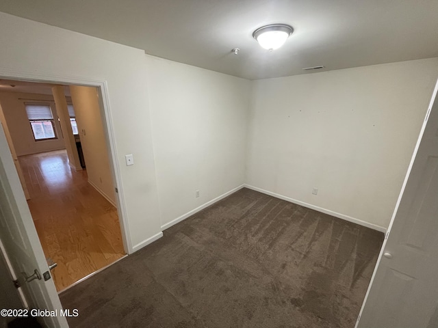spare room featuring baseboards, dark colored carpet, and visible vents