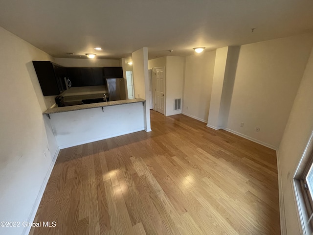 kitchen with light countertops, light wood-style floors, visible vents, freestanding refrigerator, and dark cabinets