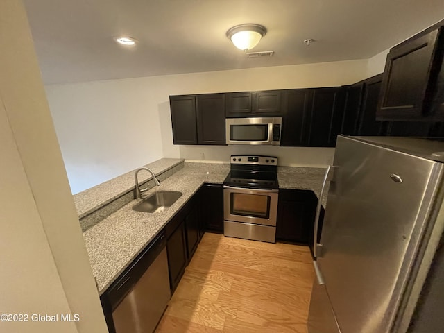 kitchen featuring visible vents, light stone countertops, stainless steel appliances, a sink, and dark cabinets