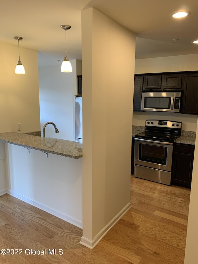 kitchen with baseboards, light stone countertops, appliances with stainless steel finishes, decorative light fixtures, and light wood-style floors
