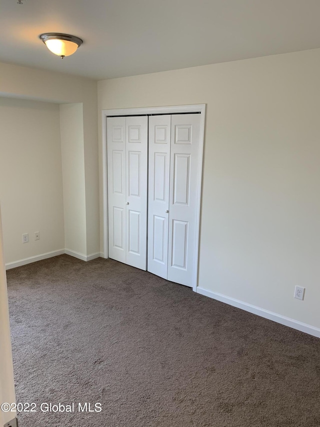 unfurnished bedroom with baseboards, a closet, and dark colored carpet