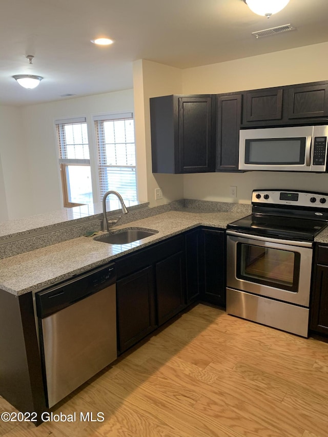 kitchen featuring stainless steel appliances, a sink, visible vents, light wood-style flooring, and a peninsula