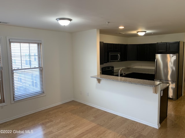 kitchen featuring light stone counters, light wood finished floors, a peninsula, appliances with stainless steel finishes, and dark cabinets