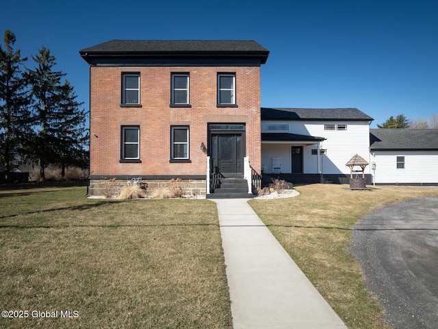 view of front of home featuring a front lawn, brick siding, and roof with shingles