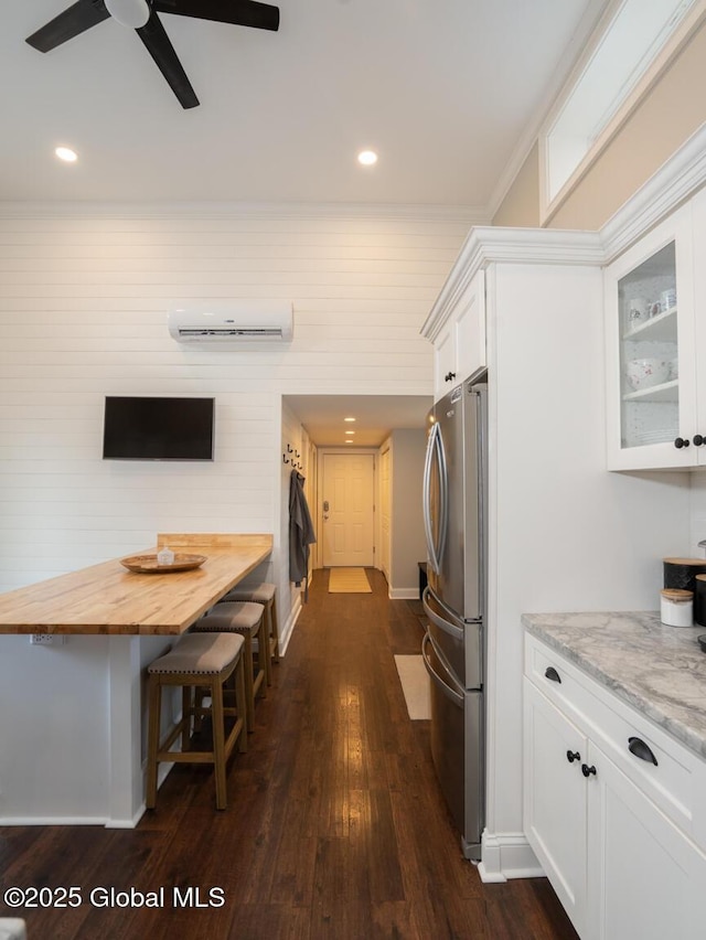 kitchen featuring dark wood-style flooring, an AC wall unit, wooden counters, freestanding refrigerator, and white cabinets