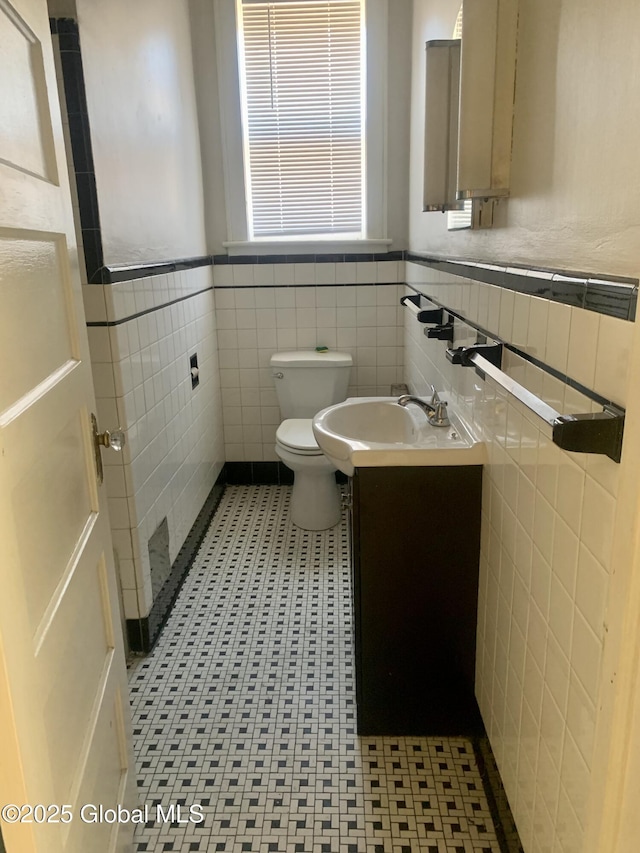 bathroom featuring tile walls, toilet, vanity, and wainscoting