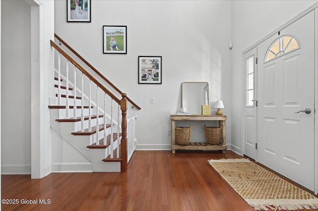 entrance foyer with stairs, a towering ceiling, baseboards, and wood finished floors