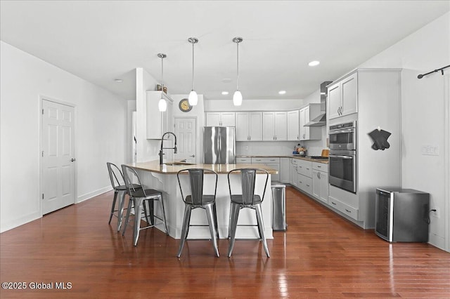 kitchen featuring a sink, a kitchen bar, dark wood finished floors, a peninsula, and stainless steel appliances