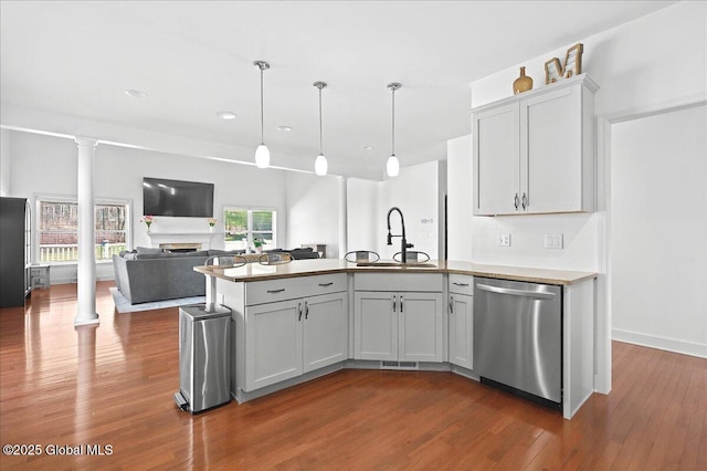 kitchen featuring a sink, dark wood-style flooring, a peninsula, a fireplace, and stainless steel dishwasher