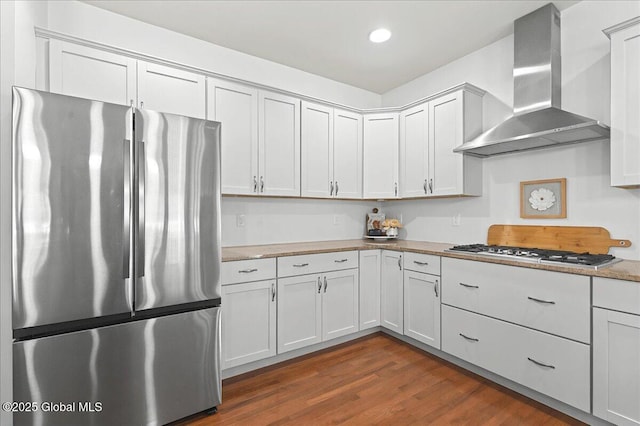 kitchen featuring dark wood-style flooring, wall chimney range hood, recessed lighting, white cabinets, and stainless steel appliances