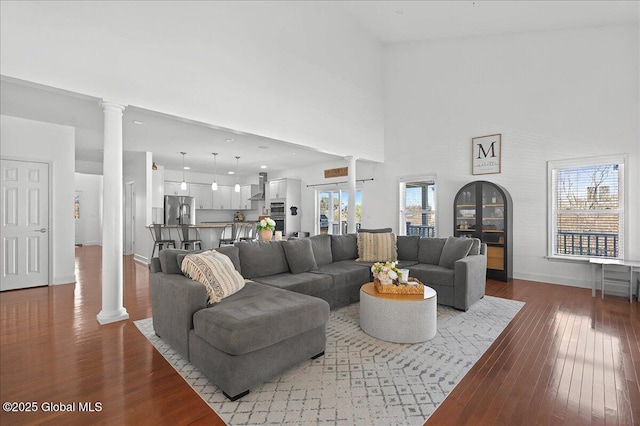 living room featuring baseboards, ornate columns, a high ceiling, and hardwood / wood-style flooring