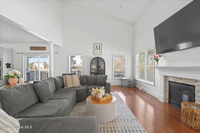 living area with visible vents, baseboards, a stone fireplace, wood finished floors, and high vaulted ceiling