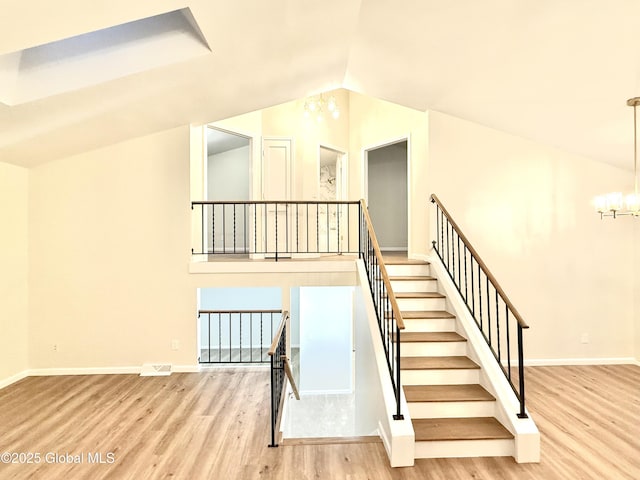 staircase featuring a notable chandelier, baseboards, vaulted ceiling, and wood finished floors