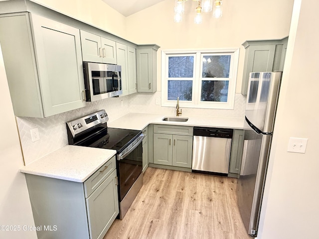 kitchen featuring gray cabinets, a notable chandelier, a sink, appliances with stainless steel finishes, and light wood-type flooring