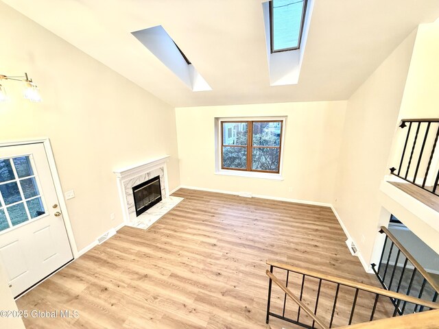 unfurnished living room with visible vents, a high end fireplace, baseboards, wood finished floors, and vaulted ceiling with skylight
