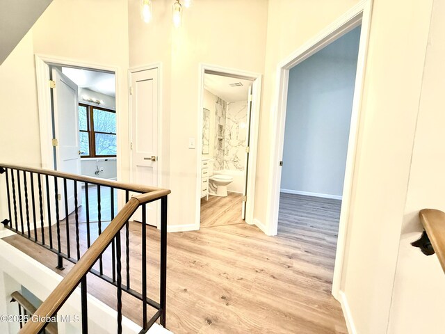 corridor with baseboards, light wood-type flooring, and an upstairs landing