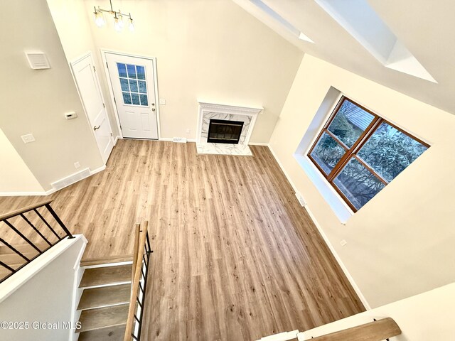 unfurnished living room featuring baseboards, high vaulted ceiling, a high end fireplace, and wood finished floors