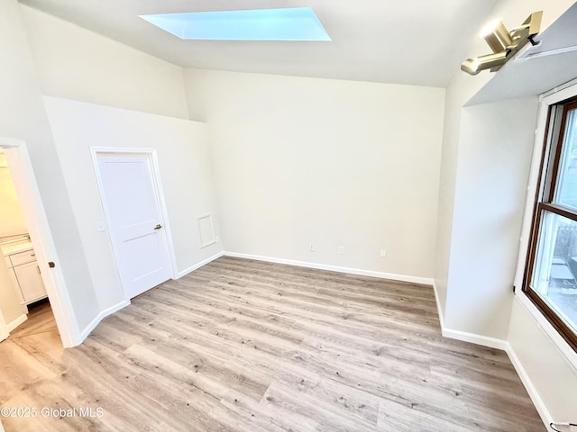 empty room featuring baseboards, vaulted ceiling with skylight, and light wood-type flooring