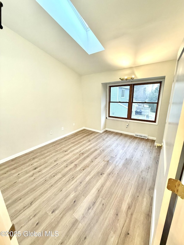 empty room featuring baseboards, visible vents, lofted ceiling with skylight, and light wood-type flooring