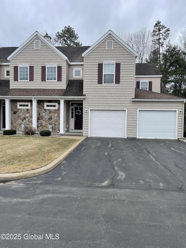 view of front of house with stone siding, a garage, a front lawn, driveway, and a shingled roof
