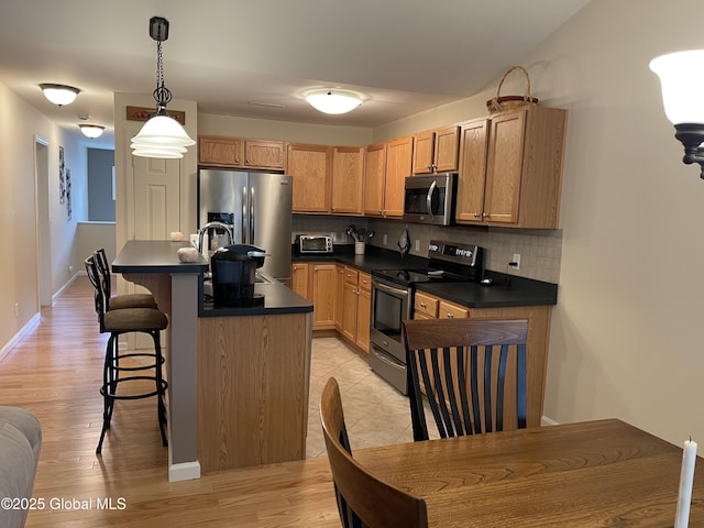 kitchen featuring light wood finished floors, a breakfast bar area, tasteful backsplash, appliances with stainless steel finishes, and dark countertops