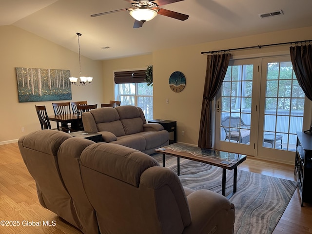 living room with lofted ceiling, baseboards, ceiling fan with notable chandelier, visible vents, and light wood-style floors