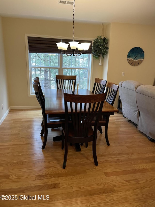 dining area with baseboards, light wood-type flooring, visible vents, and an inviting chandelier