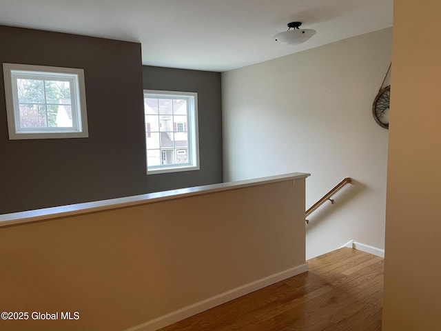 hall featuring baseboards, wood finished floors, and an upstairs landing