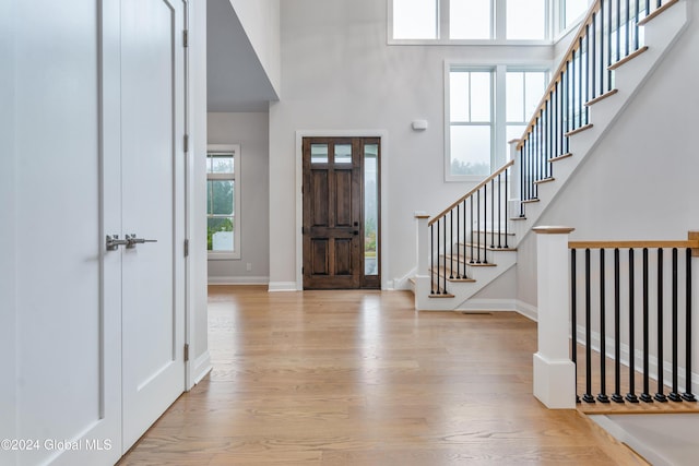foyer with baseboards, a high ceiling, stairway, and wood finished floors