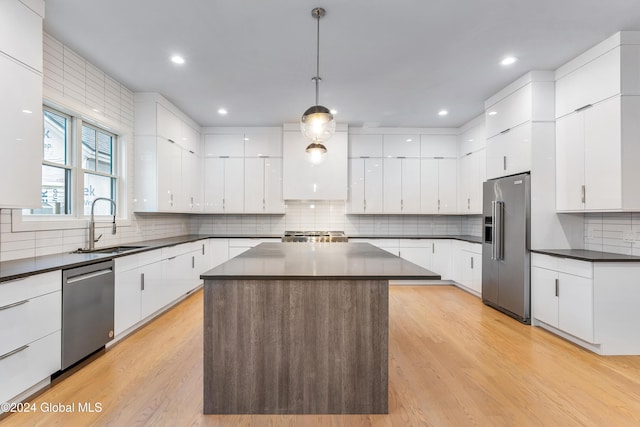 kitchen with a sink, appliances with stainless steel finishes, modern cabinets, light wood-type flooring, and dark countertops