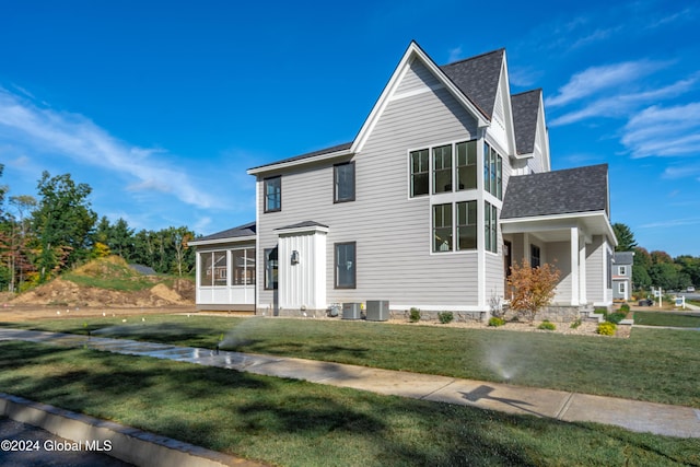 view of front of property with a sunroom, central air condition unit, board and batten siding, a front lawn, and a shingled roof