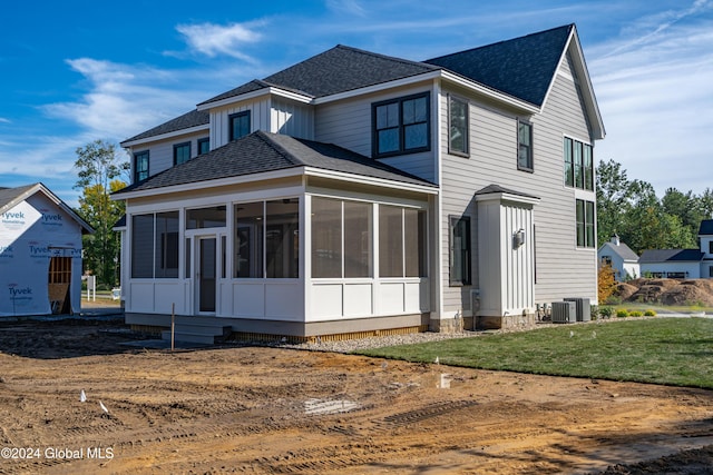 view of front of home with cooling unit, a sunroom, roof with shingles, and a front lawn