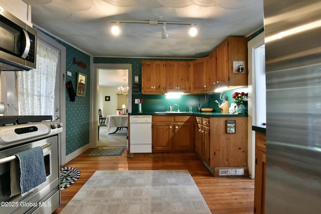 21 Andrews St, Saratoga Springs, NY 12866 - kitchen with a sink, wood finished floors, appliances with stainless steel finishes, brown cabinets, and wallpapered walls