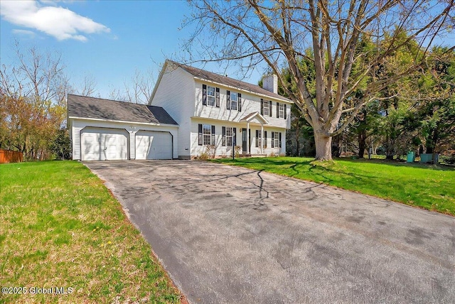 colonial house with a garage, a front yard, driveway, and a chimney