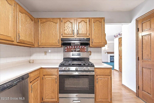kitchen with decorative backsplash, light countertops, under cabinet range hood, stainless steel appliances, and light wood-style flooring