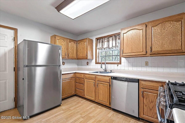 kitchen featuring appliances with stainless steel finishes, a sink, light wood finished floors, light countertops, and decorative backsplash