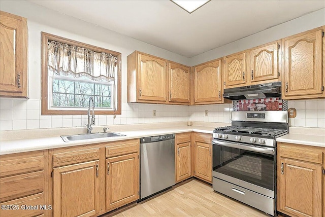 kitchen featuring light countertops, under cabinet range hood, tasteful backsplash, a sink, and appliances with stainless steel finishes
