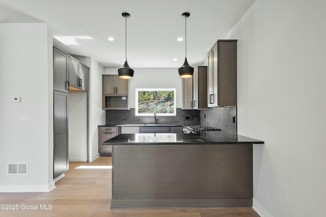 kitchen with light wood finished floors, a peninsula, visible vents, and tasteful backsplash