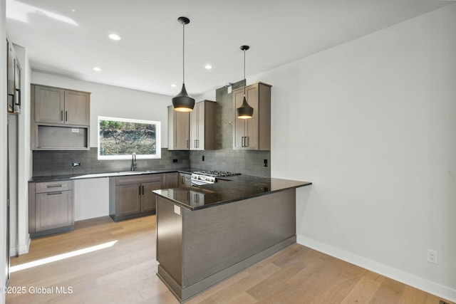 kitchen with light wood-type flooring, a peninsula, a sink, and backsplash