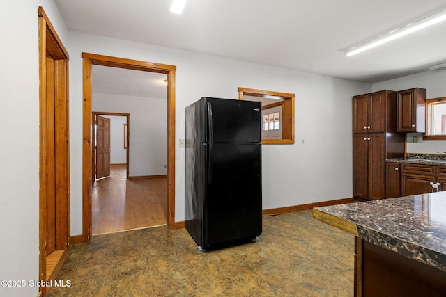 kitchen featuring freestanding refrigerator, dark stone counters, and baseboards