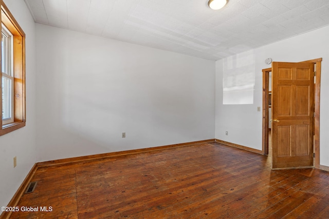 empty room with hardwood / wood-style floors, baseboards, and visible vents