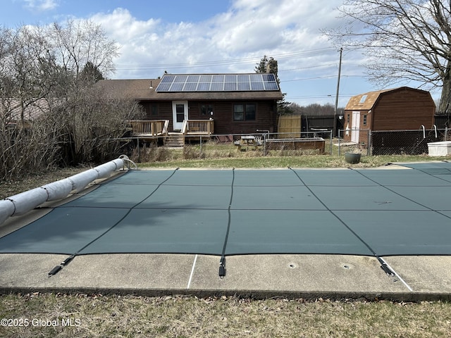 rear view of house featuring solar panels, a deck, a covered pool, and fence